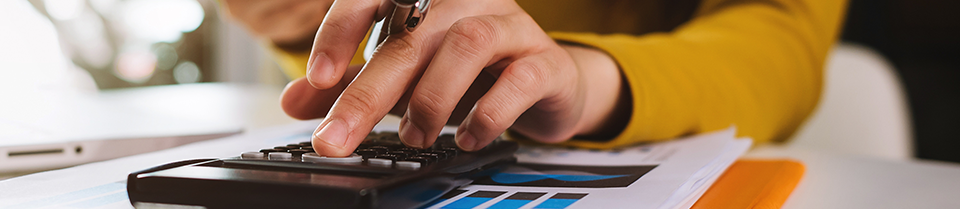 Banner image of a person's hand as they use a calculator.